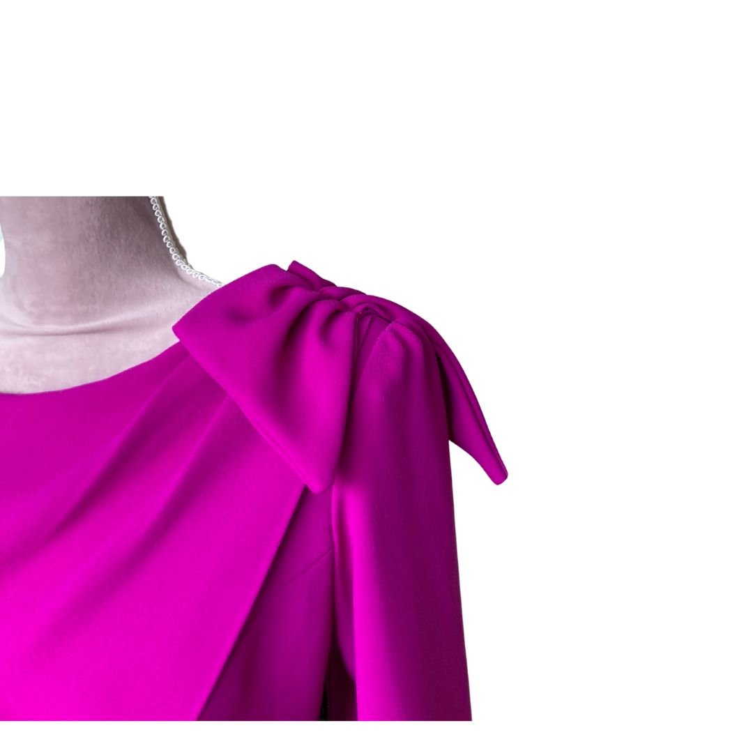 This fitted dress in high quality fuchsia crepe has a flattering drape across the bust that extends over the shoulder in a Bow detail and down the back creating a little extra drama for a special occasion. The dress has ¾ sleeves and is fully lined in satin with a back zip. 