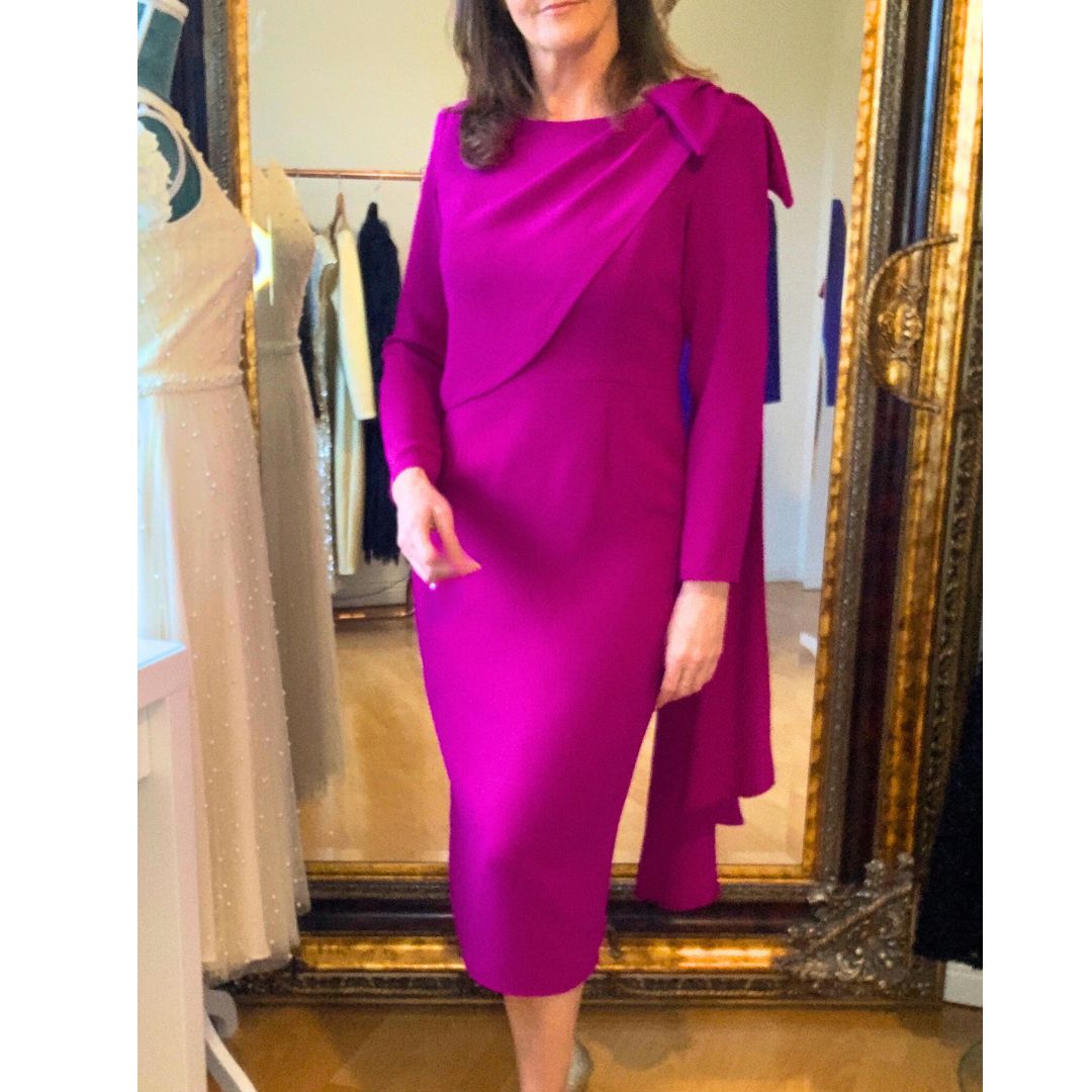 This fitted dress in high quality fuchsia crepe has a flattering drape across the bust that extends over the shoulder in a Bow detail and down the back creating a little extra drama for a special occasion. The dress has ¾ sleeves and is fully lined in satin with a back zip. 