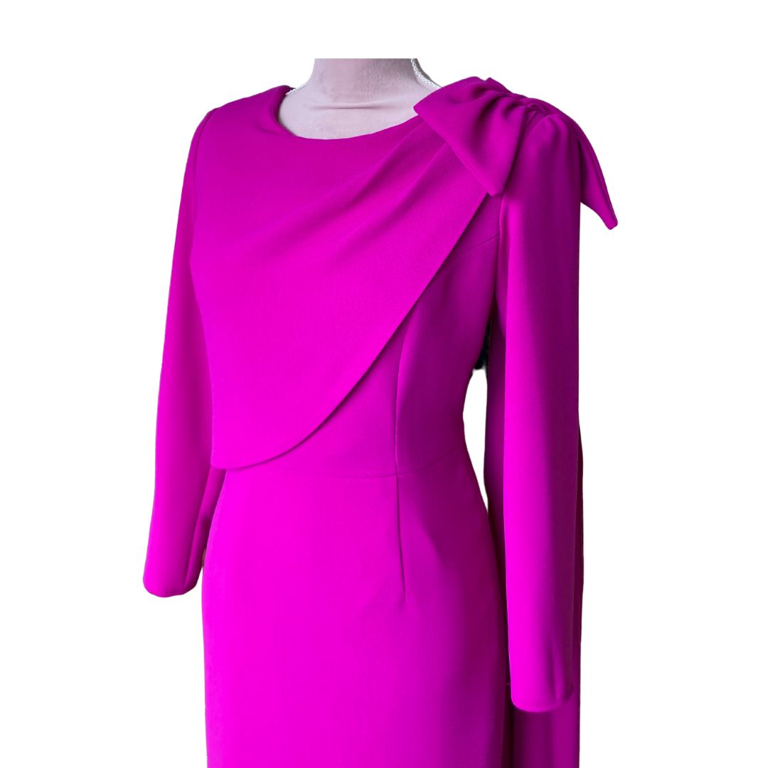 This fitted dress in high quality fuchsia crepe has a flattering drape across the bust that extends over the shoulder in a Bow detail and down the back creating a little extra drama for a special occasion. The dress has ¾ sleeves and is fully lined in satin with a back zip. 