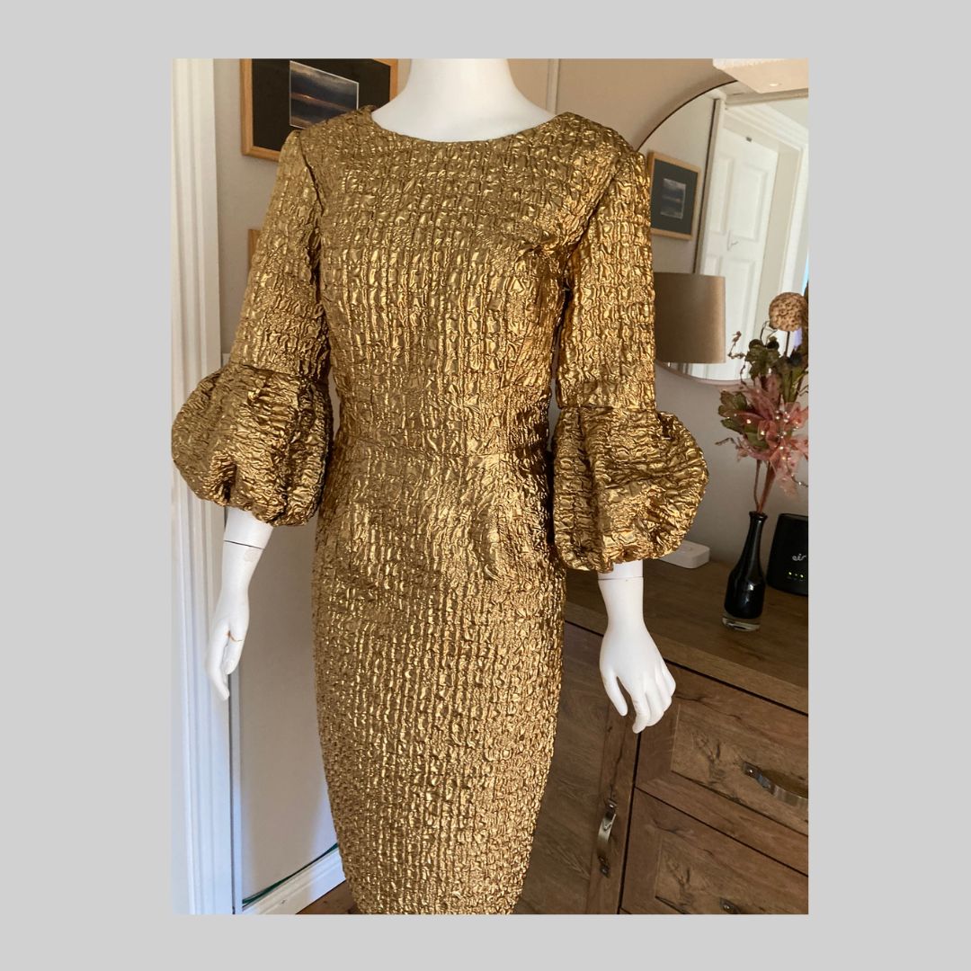 This Metallic Gold Embossed Jacquard Shift Dress gives a very simple line while offering a unique twist with a volume cuff. The luxurious fabric is incredibly lightweight, and the metallic finish elevates the dress to a special occasion. Fully Lined in Satin with concealed zip at the back.