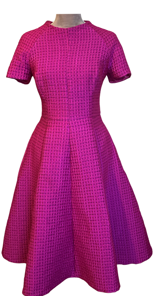  This Vintage Inspired High Neck Dress is created in a Geometric Texture Jacquard in a vibrant Magenta colour.   The full swing skirt is nipped in waist to create a very flattering silhoutte while the high neckline adds a demure elegance